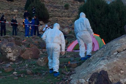 Zwei Menschen in weißen Overalls nähern sich einem bunten Zelt, das zwischen Felsen steht