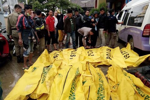Eine Gruppe Männer steht vor etwa zwölf knallgelben Leichensäcken, in denen Todesopfer des Tsunamis liegen
