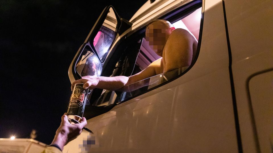 Ein Lkw-Fahrer, dem ein Bier gereicht wird