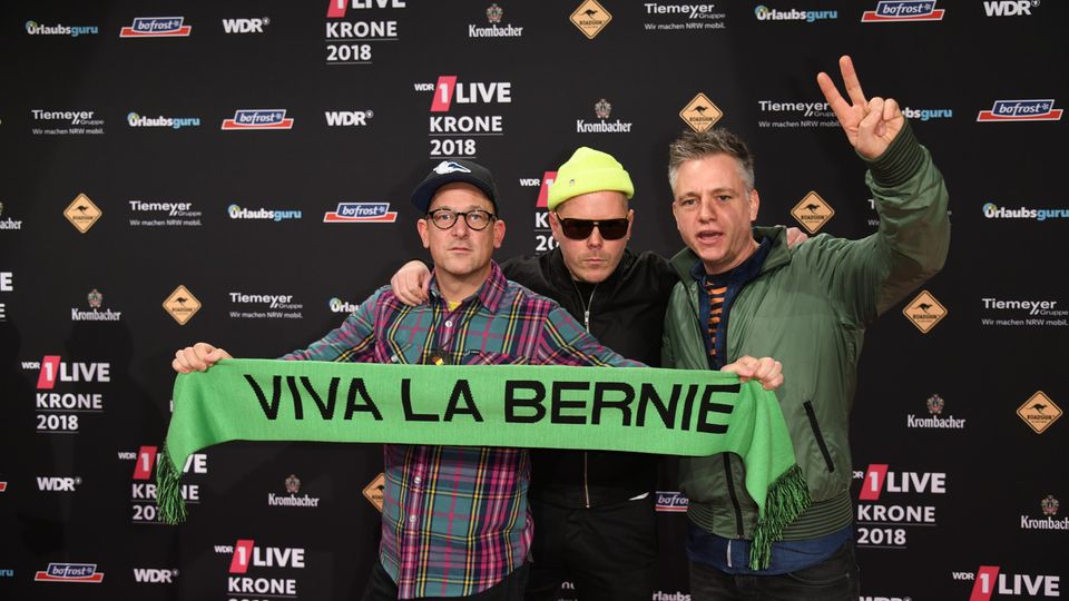 Die drei Mitglieder von "Fettes Brot" posieren mit einem grünen Schal mit "Viva la Bernie"-Schriftzug