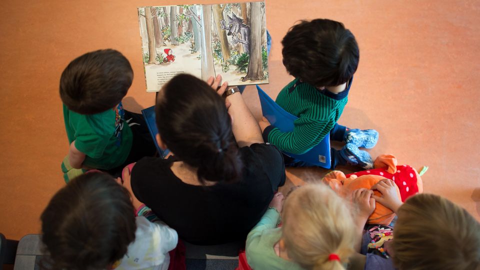 Eine Kita-Mitarbeiterin liest Kindern ein Buch vor
