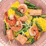 Safran-Spargel-Risotto mit Garnelen und Lachs      Zutaten:   8 rohe Garnelen (à ca. 20 g; ohne Kopf, mit Schale; frisch oder tiefgekühlt), 200 g grüner Spargel, 1 Lachsfilet (ca. 100 g), 1 kleine Zwiebel, 30 g Butter, 125 g Rundkornreis (Arborio), ½ Döschen gemahlener Safran, 50 ml trockener Weißwein, etwa 500 ml heißer Fischfond, Salz, frisch gemahlener schwarzer Pfeffer, 20 g Parmesan      Zubereitung:  Die Garnelen ggf. auftauen lassen. Den Spargel waschen, die Enden abschneiden, das untere Drittel schälen und jede Stange schräg in etwa vier Stücke schneiden. Die Garnelen waschen, trockentupfen und auf der Unterseite mit einer kleinen Schere einschneiden. Die Schale bis auf das letzte Segment mit dem Schwanzfächer rundherum mit den Fingern ablösen und den Darm entfernen. Den Lachs waschen, trockentupfen und in mundgerechte Stücke schneiden. Die Zwiebel abziehen und fein würfeln. 20 g Butter in einem Topf erhitzen und die Zwiebelwürfel darin glasig anschwitzen. Den Reis zufügen und ebenfalls glasig anschwitzen. Den Safran einrühren und mit dem Weißwein ablöschen. Nach und nach den Fischfond angießen und unter Rühren einkochen lassen. Das Risotto insgesamt etwa 20 Minuten garen. Die übrige Butter in einer Pfanne erhitzen, die Spargelstücke darin etwa 8 Minuten garen, mit Salz und Pfeffer würzen und herausnehmen. Die Garnelen und den Lachs im Bratfett 3–4 Minuten braten und ebenfalls mit Salz und Pfeffer würzen. Den Parmesan reiben, unter das Risotto rühren und das Risotto würzen. Das Risotto auf Tellern anrichten, den Spargel, die Garnelen und den Lachs daraufsetzen und servieren.      Mehr Rezepte finden Sie in: Sporternährung für jeden Tag, 240 Seiten, 29,99 Euro