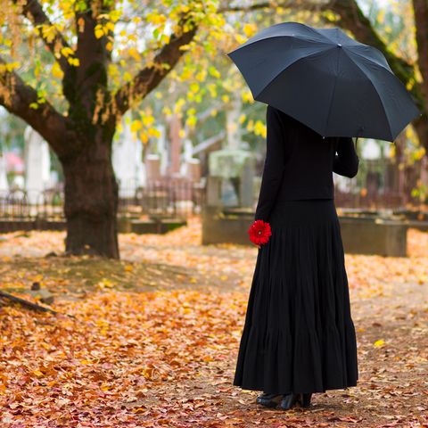 Eine mysteriöse Frau, steht einsam abseits bei einer Beerdigung