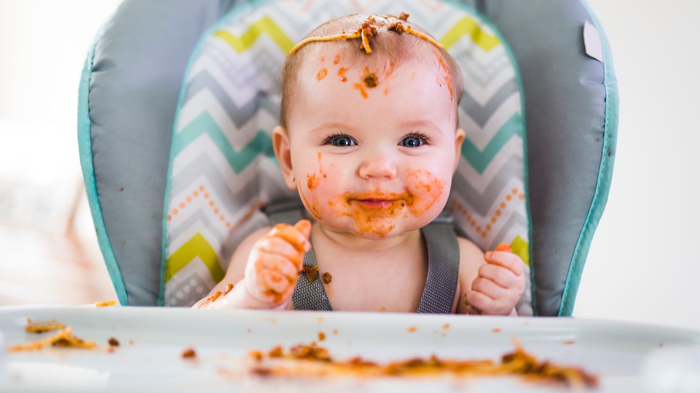 Ein tomatensoßenverschmiertes Baby lächelt glücklich in die Kamera