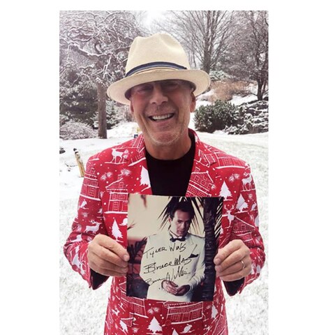 Bruce Willis steht in einem bunt gemusterten Weihnachts-Jackett vor der Haustür