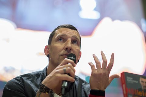 Ex-Handballer Stefan Kretzschmar sitzt auf einer Bühne und spricht in ein Mikro in seiner rechten Hand