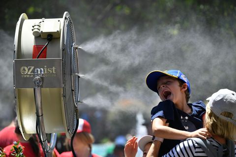 Ein Kind hält sein Gesicht in einen Ventilator, der auch Wassertröpchen versprüht
