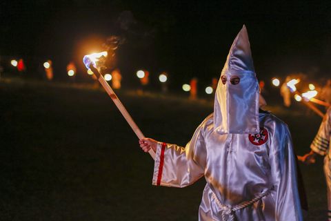 Ein Mitglied des Ku Klux Klan hält eine Fackel in der rechten Hand, während er das weiße Gewand und Mütze des Klans trägt