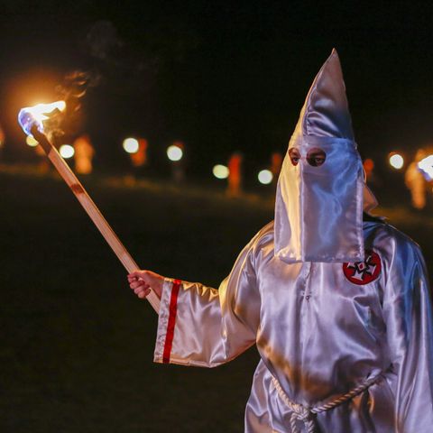 Ein Mitglied des Ku Klux Klan hält eine Fackel in der rechten Hand, während er das weiße Gewand und Mütze des Klans trägt
