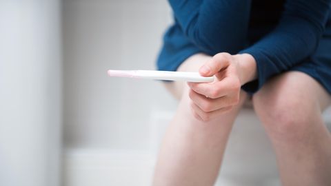 Frau auf Toilette mit Schwangerschaftstest