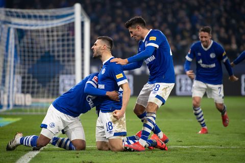 Drei Schalker Spieler knien neben dem Tor und jubeln über einen Treffer