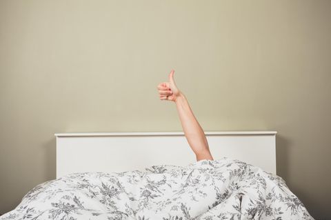 Eine Frau liegt im Bett und hält den ausgestreckten Daumen nach oben