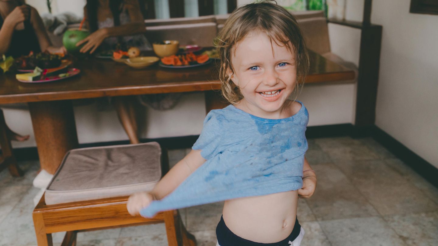 Ein kleines Mädchen mit vollgekleckertem T-Shirt lacht in die Kamera