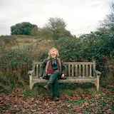 Ein älterer Mann sitzt auf einer Parkbank und schaut in den Himmel