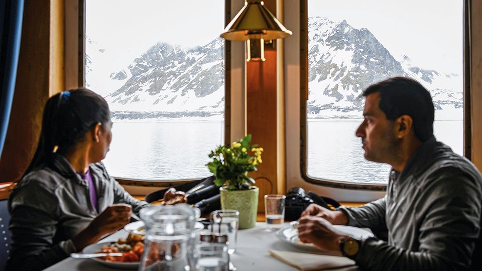 Während Swati und Karan aus Indien an Bord essen, blicken sie auf schneebedeckte Berge