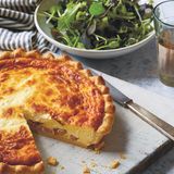 Quiche Lorraine      Zutaten:  Mürbeteig, 5 dicke Scheiben Speck (insgesamt 150 g), roh oder geräuchert, in kurze Streifen geschnitten, 4 große Eier, 180 g Crème fraîche, 360 ml Vollmilch, ⅛ TL frisch gemahlener schwarzer Pfeffer, ⅛ TL frisch gemahlene Muskatnuss, 55 g dicke Schinkenscheiben, gewürfelt      Mürbeteig: 200 g Weizenmehl (Type 405), plus mehr zum Ausrollen, ½ TL feines Meersalz, 100 g kalte Butter, gewürfelt, 1 großes Ei, eiskaltes Wasser, wenn nötig      Zubereitung:  Den Mürbeteig zubereiten (oder kaufen) und eine Quiche- oder Tarte-Pfanne mit einem Durchmesser von 25 cm damit auskleiden.  Den Backofen auf 200 °C vorheizen.  Den Teig in der Quiche-Pfanne mit einem Backpapier abdecken und Backkugeln (oder getrocknete Bohnen) darauf verteilen. 15 Minuten blindbacken.  In der Zwischenzeit in einer kleinen, trockenen Pfanne die Speckstreifen etwa 10 Minuten, oder bis sie leicht angebräunt sind, anbraten. Herausschöpfen. (Das ausgelassene Fett für andere Rezepte aufbewahren.)  In einer mittelgroßen Schüssel die Eier mit einer Gabel vorsichtig verquirlen. Behutsam die Crème fraîche, die Milch, den Pfeffer und die Muskatnuss einrühren. Es sollte nicht zu viel Luft in die Mischung gerührt werden, sonst bilden sich Blasen in der Füllung, die beim Backen zu Rissen führen.  Den Quicheboden aus dem Backofen holen und die Temperatur auf 150 °C reduzieren. Das Backpapier vorsichtig anheben und die Backkugeln entfernen.  Den Speck und den Schinken gleichmäßig auf dem Quicheboden verteilen und dann langsam die Eiermischung darübergießen. Darauf achten, dass der Speck und der Schinken gleichmäßig verteilt bleiben. 50–60 Minuten, oder bis die Füllung goldbraun, aber in der Mitte noch ein wenig dickflüssig ist, backen. Vor dem Servieren mindestens 15 Minuten fest werden lassen. Warm oder zimmerwarm mit dem Salat genießen.