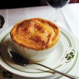 Pariser Zwiebelsuppe      Zutaten:  15 g Butter, 1 EL Olivenöl, 560 g gelbe Zwiebeln, fein geschnitten, 1 TL feines Meersalz, 2 EL Weizenmehl, Type 405, 120 ml trockener Weißwein (alternativ Bier oder halb Portwein, halb Wasser), 960 ml Rinderbrühe, vorzugsweise selbst gemacht, 1 EL Rotweinessig, 4 Scheiben Brot mit Kruste (ca. 1,25 cm dick), auf die Größe der Suppenschüssel zugeschnitten, 150 g frisch geriebener Käse, wie Comté oder Gruyère, frisch gemahlener schwarzer Pfeffer, frisch gemahlene Muskatnuss      Zubereitung:  In einem Topf mit schwerem Boden bei mittlerer Temperatur die Butter und das Öl erhitzen. Die Zwiebeln und das Salz dazugeben und verrühren. Unter Rühren 30–35 Minuten, oder bis die Zwiebeln stark karamellisiert sind, kochen. Wenn sie am Boden haften bleiben, 1 EL Wasser dazugeben und die am Boden haftenden Stücke abschaben. Das Mehl einrühren. Den Wein und die Brühe hinzugeben, den Boden des Topfes abschaben und zum Köcheln bringen. Den Topf abdecken und die Suppe 15 Minuten kochen. Den Essig einrühren, die Suppe probieren und abschmecken. (Die Suppe kann bis zu einem Tag im Voraus zubereitet werden.) Auskühlen lassen, abdecken und kalt stellen. Vor dem Weiterverarbeiten aufwärmen.      Den Grill vorheizen.      Die Suppe auf 4 Schüsseln verteilen. Die Schüsseln auf ein tiefes Backblech stellen. In jede Schüssel ein Stück Brot legen und mit je 6 EL Käse bestreuen. Unter den Grill stellen und im Auge behalten. 4–5 Minuten, oder bis der Käse goldgelb ist und brodelt, grillen. Mit dem schwarzen Pfeffer und der Muskatnuss würzen.      Die Schüsseln auf einen hitzebeständigen Teller stellen und servieren. Die Gäste warnen, dass die Schüsseln heiß sind.