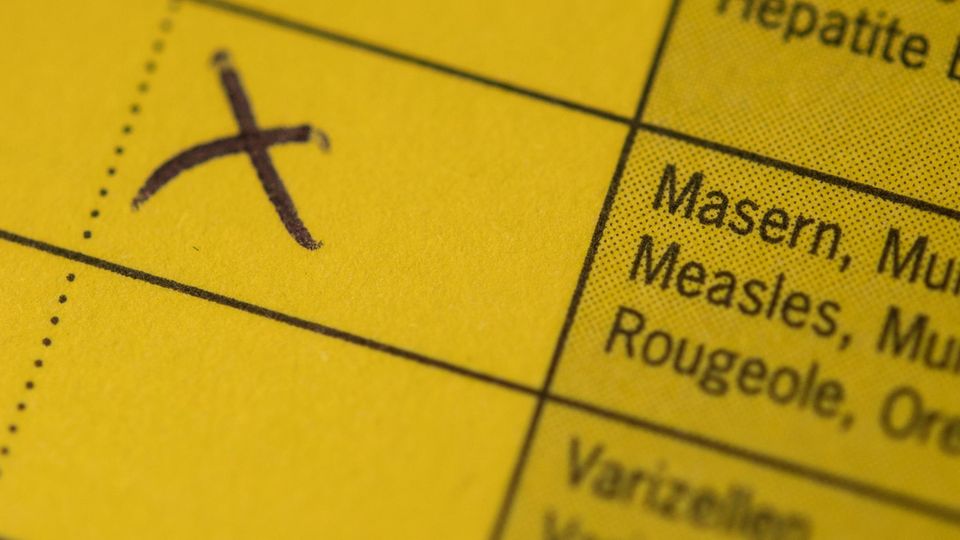 Ein Kreuz steht am auf einem Impfpass, in dem eine Kombiimpfung für Masern, Mumps und Röteln eingetragen ist