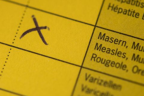 Ein Kreuz steht am auf einem Impfpass, in dem eine Kombiimpfung für Masern, Mumps und Röteln eingetragen ist