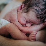 Ein frisch geborenes Babyliegt zusammengerollt auf der Brust der Mutter