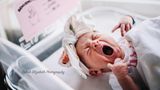 Ein Baby mit einem geknoteten Kopftuch gähnt herzhaft