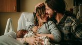 Eine Mutter stillt ihr Baby, der Vater schmust mit ihr
