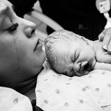 Eine stark geschminkte Mutter hält weinend ihr Baby im Arm