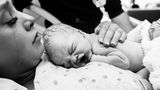 Eine stark geschminkte Mutter hält weinend ihr Baby im Arm