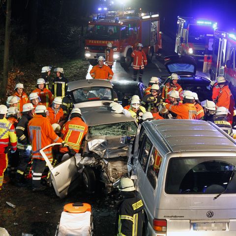 Einsatzkräfte der Feuerwehr stehen nach der Kollision eine Transporters und eines Pkw neben den Wracks