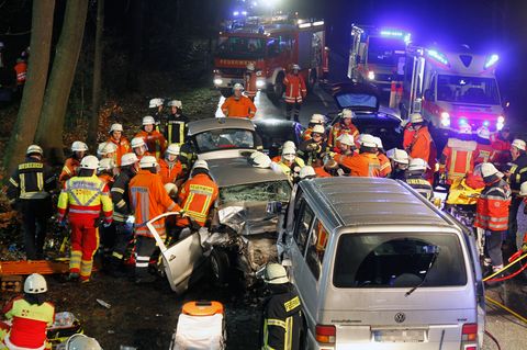 Einsatzkräfte der Feuerwehr stehen nach der Kollision eine Transporters und eines Pkw neben den Wracks