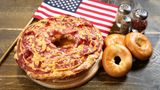 London, Vereinigtes Königreich. Sie sehen: eine Bagelizza. Eine was? Eine Mischung aus Bagel und Pizza, die eine Bäckerei in der britischen Hauptstadt an Passanten verteilt. Der Grund für die Aktion (und die eigenwillige, 1,5 Kilo schwere Kreation): Am Samstag wird nicht nur der National Pizza Day, sondern auch der National Bagel Day gefeiert.