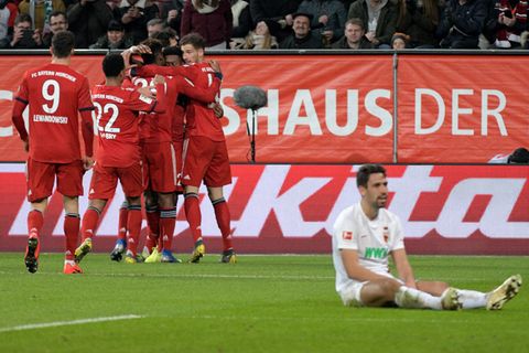 Augsburgs Rani Khedira (r.) sitzt niedergeschlagen auf dem Rasen, während die Bayern-Spieler jubeln