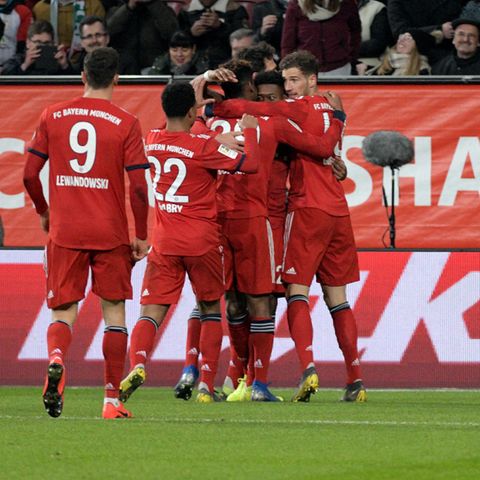 Augsburgs Rani Khedira (r.) sitzt niedergeschlagen auf dem Rasen, während die Bayern-Spieler jubeln