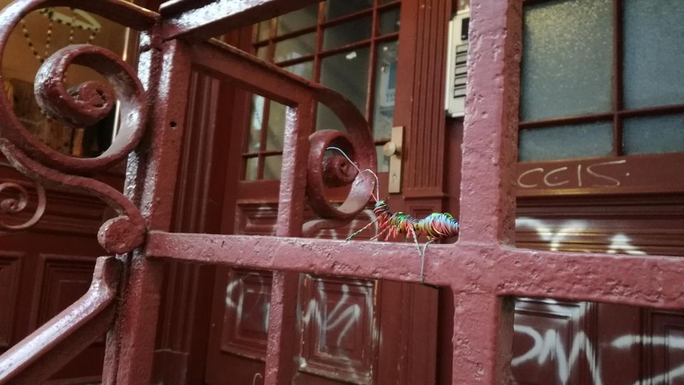 Streetart ant__works Eine Drahtameise sitzt auf einem Türgatter