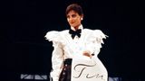 Karl Lagerfeld wurde 1983 Kreativdirektor von Chanel. Er lehnte seine Designs an die Kreationen von Coco Chanel an – nur eben moderner. Das französische Model Ines de la Fressange zeigt sich hier in einem Look der Herbst/Winter-Kollektion von 1984/1985 in Paris, einer der ersten Kollektionen von Karl Lagerfeld für Chanel. Sie präsentiert einen klassischen, aber trotzdem spannenden Chanel-Look in schwarz-weiß. Details wie Schulterpolster und Rüschen, Schleife und die großen Perlen-Ohrringe sind charakteristisch für das Modehaus.