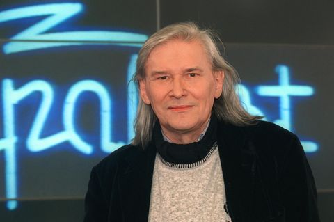 Vor einem Neon-Schriftzug" Rockpalast" schaut Peter Rüchel mit grauen, schulterlangen Haaren in die Kamera