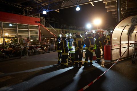 Mehrere Feuerwehrleute stehen im Scheinwerferlicht auf dem Parkplatz eines Einkaufszentrum in Unkel