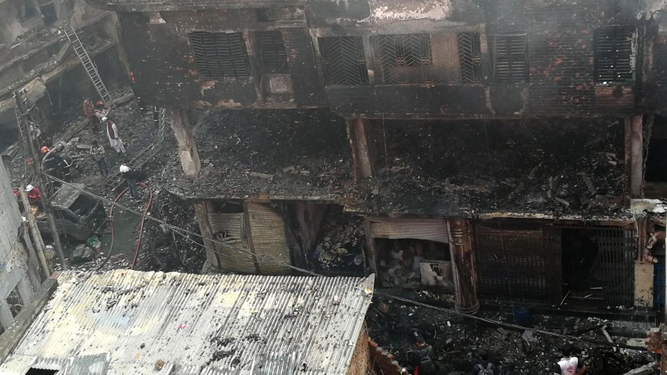 Menschen stehen nach einem Brand in der Nähe eines von den Flammen zerstörten Gebäudes in Bangladeschs Hauptstadt Dhaka