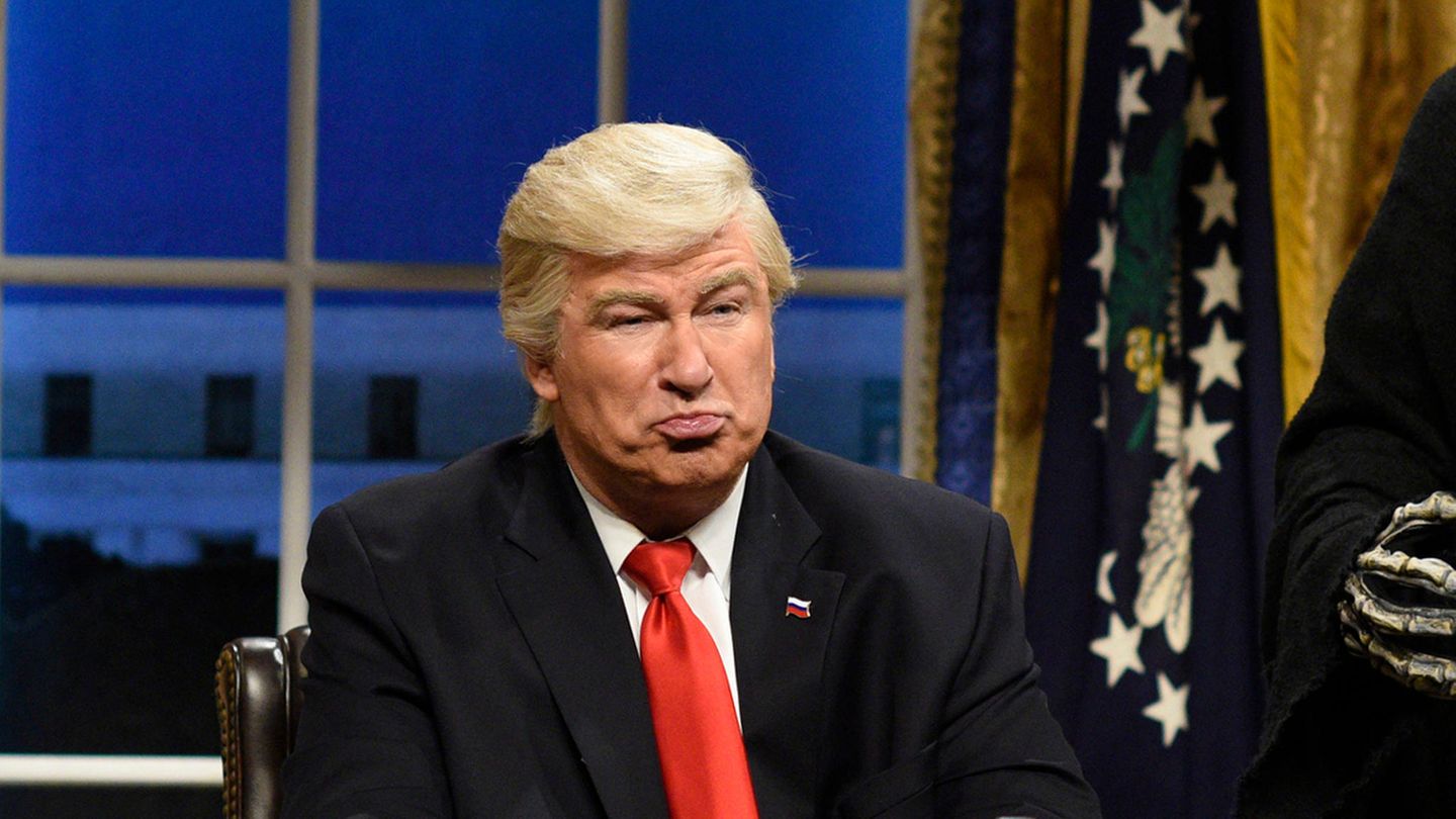 Schauspieler Alec Baldwin sitzt als Donald Trump in einer Kulisse, die ans Oval Office erinnert