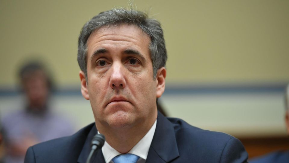 Michael Cohen Michael Cohen sitzt in Anzug und Krawatte vor einem Mikrofon und scheint gerade einer Frage zu lauschen