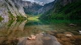 Obersee, Berchtesgaden, Bayern  Wie eine Spiegelung der Felsen rund um den See erscheint die Wasseroberfläche des Obersees. Das sehr klare Wasser des Sees macht das möglich. Da es keinen Bootsverkehr auf dem See gibt und er geschützt liegt, wird dieser Effekt noch verstärkt. Die Wanderwege rund um den Obersee führen auch zum nördlich gelegenen Königssee. Dieser ist durch einen Moränenwall vom Obersee getrennt.