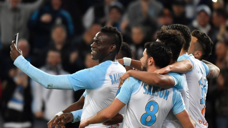 Mario Balotelli Fußballer in hellblau-weißen Trikots von Olympique Marseille stehen in einer Gruppe zusammen. Einer hält ein Smartphone hoch