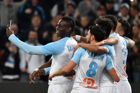 Fußballer in hellblau-weißen Trikots von Olympique Marseille stehen in einer Gruppe zusammen. Einer hält ein Smartphone hoch