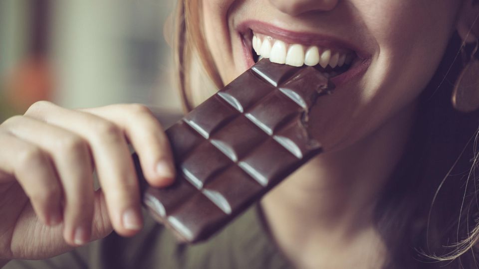 Frau, die mit einem Lächeln in Schokolade beißt
