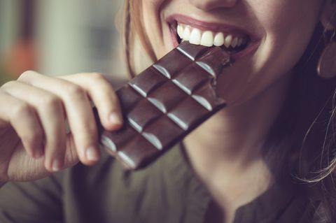 Frau, die mit einem Lächeln in Schokolade beißt