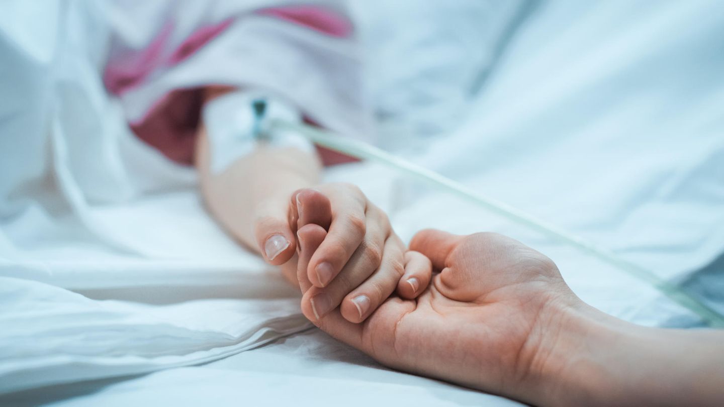 Eine Person hält einer kranken Person im Krankenbett die Hand