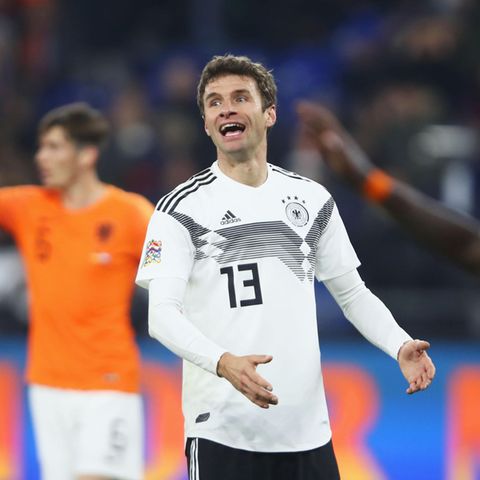 Thomas Müller gestikuliert im DFB-Trikot auf dem Platz. Im Hintergrund stehen zwei Spieler der Niederlande