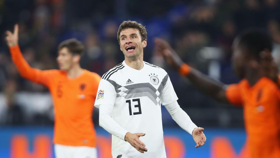 Thomas Müller gestikuliert im DFB-Trikot auf dem Platz. Im Hintergrund stehen zwei Spieler der Niederlande