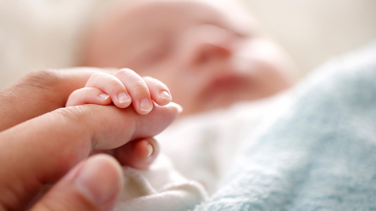 Hand eines Erwachsenen hält die Finger eines grade geborenen Babys