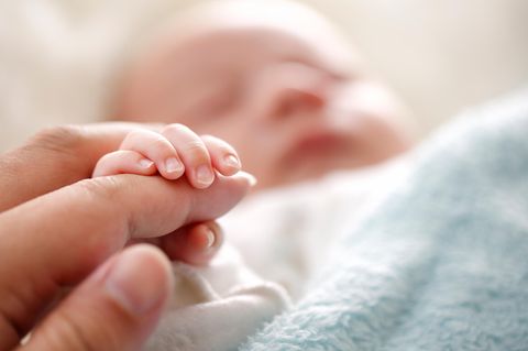 Hand eines Erwachsenen hält die Finger eines grade geborenen Babys